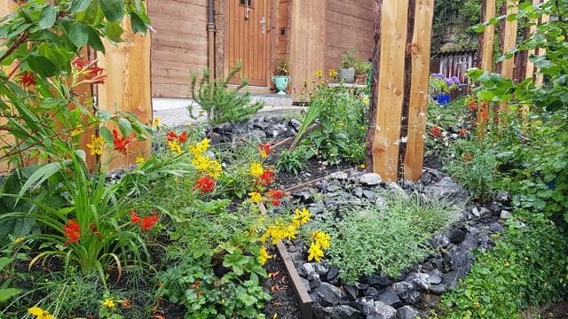 Blühendes Staudenbeet mit Steinen vor einem Holzhaus